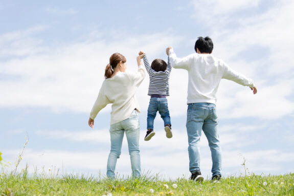 若い家族の全身後ろ姿、青空背景